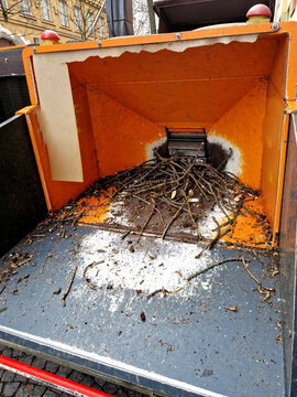 intake area hopper of a large, industrial-looking, typically truck-mounted or trailer-mounted wood chipper. The dominant color is orange. There are small branches and sticks piled , composting