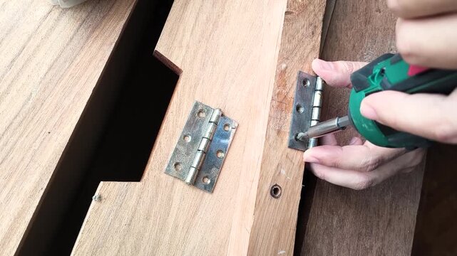 Craftsman attaching hinges to wooden structure with power screwdriver. Focus on skill, repair, and DIY home improvement. Perfect for home repair, construction and projects.