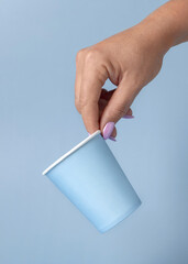 Female hand with disposable light blue paper cup closeup, mockup, copy space. Single-use cup