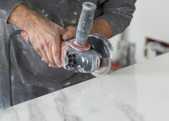 Craftman in grey shirt cuts a gray marble tile using an angle grinder. Handy men at work, hands closeup