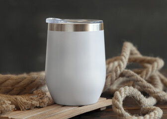 White blank Stainless Steel tumbler on dark wood against rustic jute ropes close up, nautical mockup