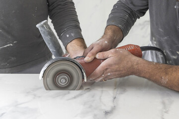 Craftman in grey shirt cuts a gray marble tile using an angle grinder. Handy men at work, hands closeup