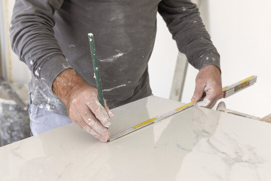 Craftman in grey shirt measures a marble tile using a ruler. Handy men at work, hands closeup