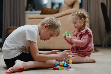 Obraz premium A 9-year-old boy with hearing aids plays naturally with his 4-year-old sister. Authentic sibling bonding moment showcasing inclusive family relationships and childhood joy