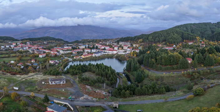 Aerial view of Pukë with its lake, colourful homes, and dense pine forests beneath dramatic evening clouds and mountain backdrops.
