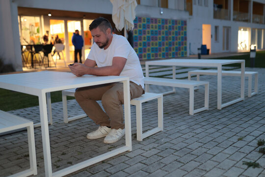 Man sitting engrossed in mobile phone at outdoor table - Powered by Adobe