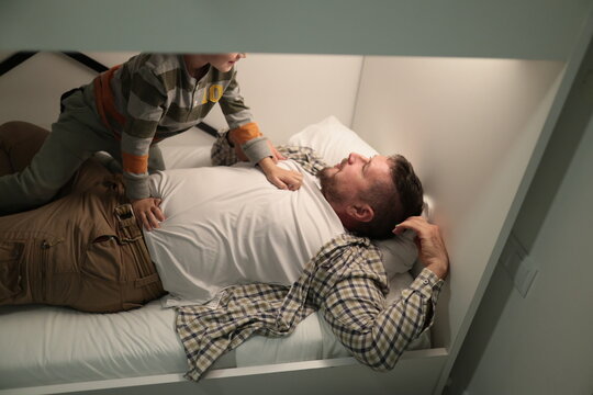 Child playing on father waking up on bed