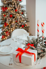 Wrapped present with red ribbon on festive table near decorated Christmas tree and lit candles