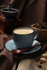 Aromatic coffee in cup, beans, brown sugar and grinder on wooden table, closeup