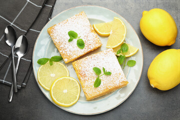 Tasty lemon bars with powdered sugar, mint and fresh fruits on grey table, flat lay