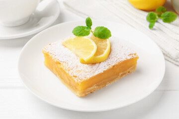 Tasty lemon bar with powdered sugar and mint on white wooden table, closeup