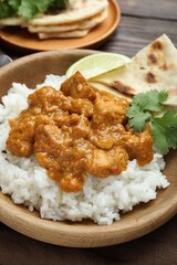 Delicious chicken tikka masala with rice, cilantro, lime and lavash in bowl on wooden table, closeup