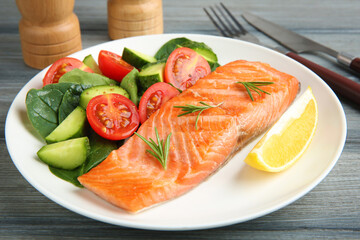 Piece of tasty grilled salmon, lemon, rosemary and salad on grey wooden table, closeup