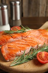Pieces of tasty grilled salmon, rosemary and tomato on wooden table, closeup