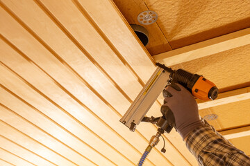 Worker using pneumatic nail gun to secure wooden ceiling panels during interior renovation, timber construction process, insulation layers, manual labour, craftsmanship and precise home improvement