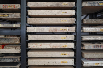 Front view of heavy limestone slabs used for lithography printing stored horizontally on a black metal rack in a workshop.