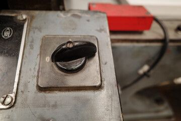 A close-up detail shot of an old black rotary switch or knob mounted on the worn grey metal panel of an industrial machine.