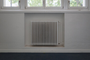 A front view of a classic white cast iron radiator installed in a recessed wall niche beneath a row...