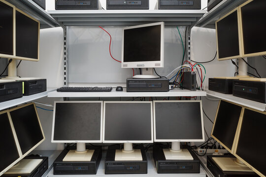 Multiple outdated desktop computers, including LCD monitors and horizontal processing units, arranged on white metal shelving.