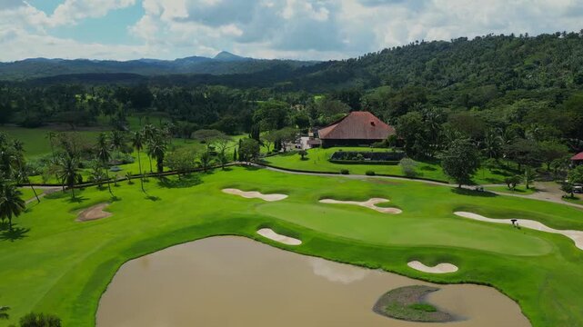 A leveled aerial moving toward the clubhouse with red roof, passing fairways and tropical trees in Canlubang Golf and Country Club, Calamba Laguna, Philippines