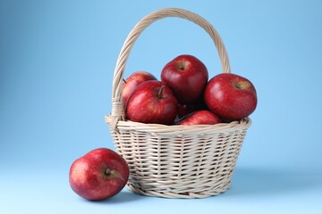 Ripe red apples and wicker basket on light blue background, closeup