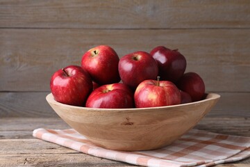 Ripe red apples in bowl on wooden table, closeup