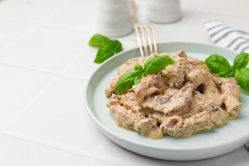 Tasty beef Stroganoff with basil on white tiled table, closeup. Space for text