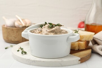 Tasty beef Stroganoff with thyme in casserole, bread and spices on white tiled table, closeup