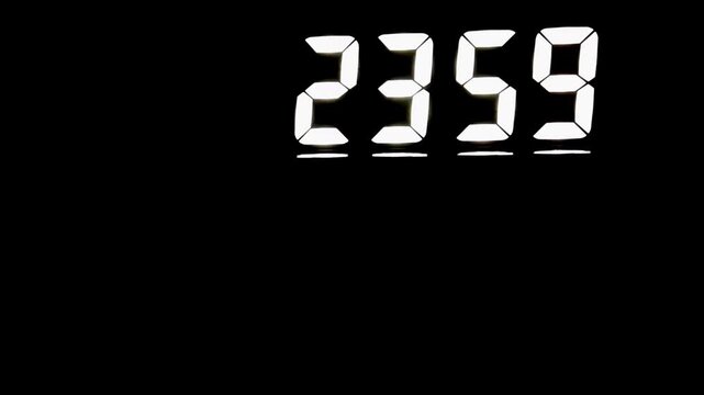 A digital clock switching from 23:59 to 00:00 in a dark room