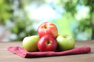Fresh red and green apples on wooden table against blurred green background, closeup