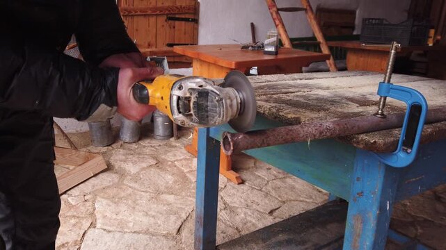 Hands of worker cutting iron pipe with cordless angle grinder