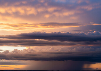 Fototapeta premium Golden hour illuminates dramatic stormy clouds over the ocean, with a distant rain shower visible as the sun sets, creating a breathtaking atmospheric landscape painting