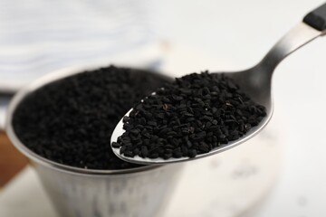 Aromatic black caraway in spoon near bowl at table, closeup