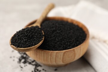 Aromatic black caraway in wooden bowl and spoon on light grey table, closeup