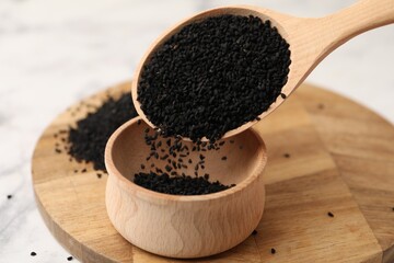 Pouring aromatic black caraway into bowl at white marble table, closeup