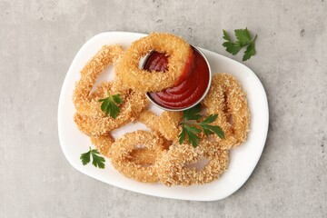 Deep fried squid rings with parsley and ketchup on grey textured table, top view