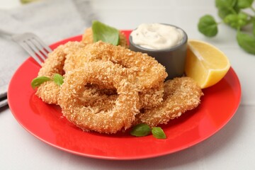 Deep fried squid rings with basil, sauce and slice of lemon on white tiled table, closeup