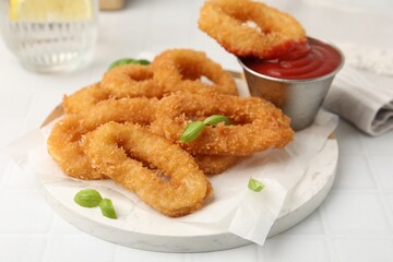 Deep fried squid rings with basil and ketchup on white tiled table, closeup