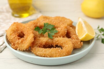 Deep fried squid rings with parsley and lemon slice on white table, closeup