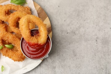 Deep fried squid rings with basil and ketchup on light grey table, top view. Space for text