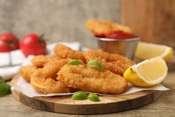 Deep fried squid rings with lemon slice, basil and ketchup on wooden table, closeup