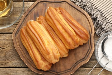 Tasty eclairs, powdered sugar and tea on wooden table, flat lay