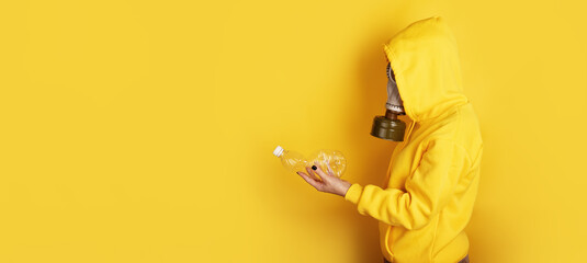 Individual in yellow hoodie and gas mask holding plastic bottle against bright yellow background....