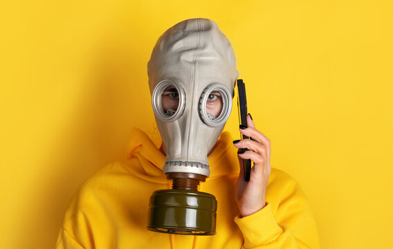 Individual wearing a gray gas mask and yellow hoodie, holding a phone to their ear against a vibrant yellow background.