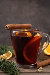 Tasty mulled wine with spices in glass cup and fir branches on wooden table, closeup