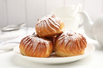 Tasty profiteroles with powdered sugar served on white wooden table, closeup