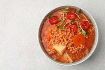 Delicious lentil soup with vegetables in bowl on light grey table, top view. Space for text