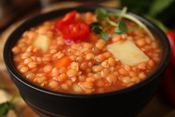 Delicious lentil soup with vegetables in bowl on table, closeup
