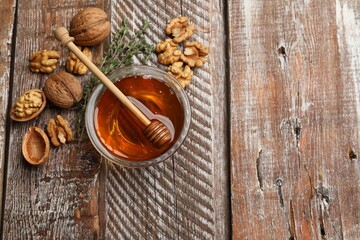 Honey in bowl, walnuts and thyme on wooden table, flat lay. Space for text