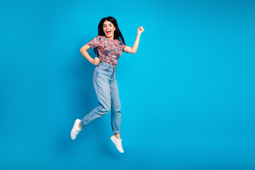 Young woman jumps with joy in casual fashion against a bright blue background